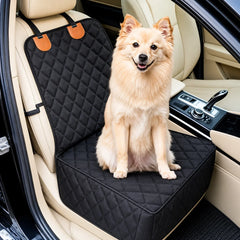 A small fluffy tan dog sits on a black quilted car seat cover installed in a beige car interior.